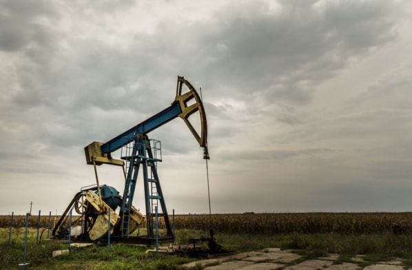A lone oil pump stands in an open field under a moody sky