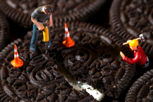 Miniature construction workers split an Oreo cookie to symbolize shrinkflation