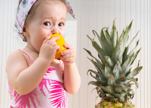 A small toddler makes a sour face as it takes a bite of a lemon.