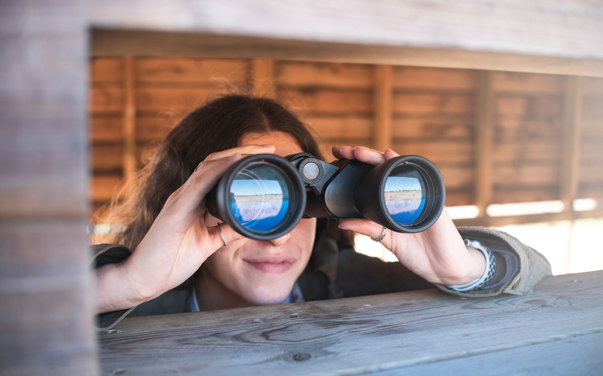 a young person gazes through a pair of binoculars