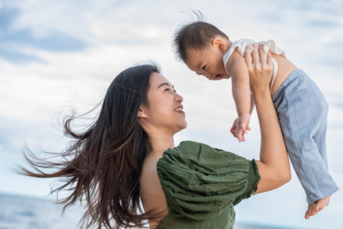 A happy mom holds her baby at the beach