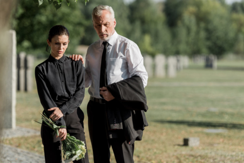 Two mourners stand in a cemetery