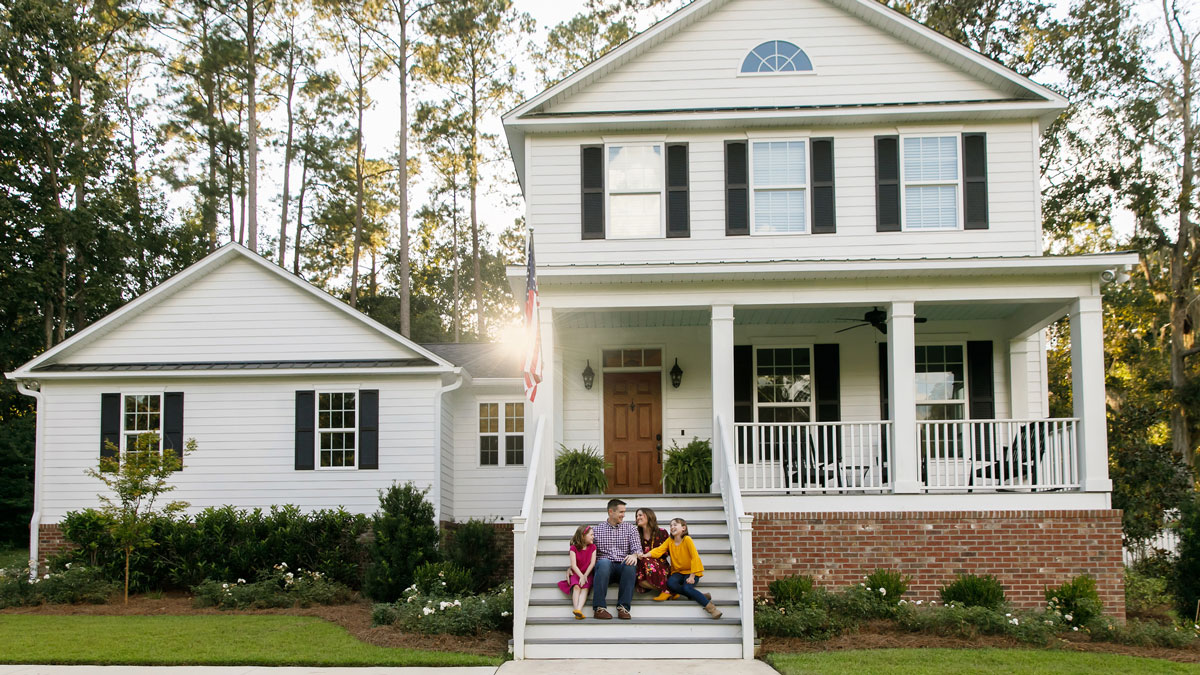 Family sitting on the steps of a large colonial home in the suburbs - family legacy planning